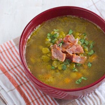 split pea soup in a red bowl with bacon on top