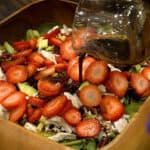 Pouring dressing over chicken salad recipe with strawberries