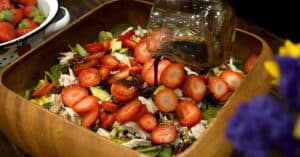Pouring dressing over chicken salad recipe with strawberries