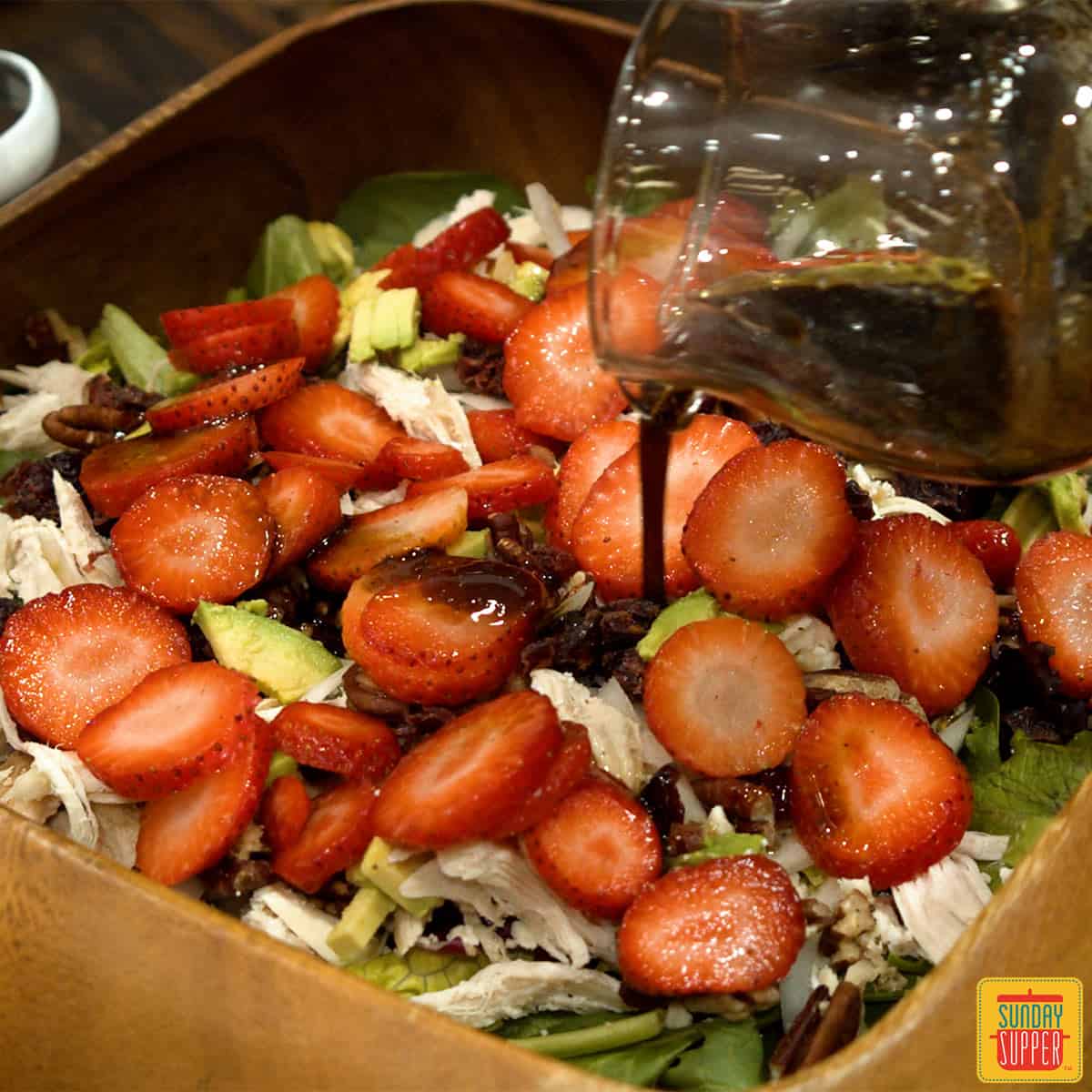 Pouring dressing over chicken salad recipe with strawberries