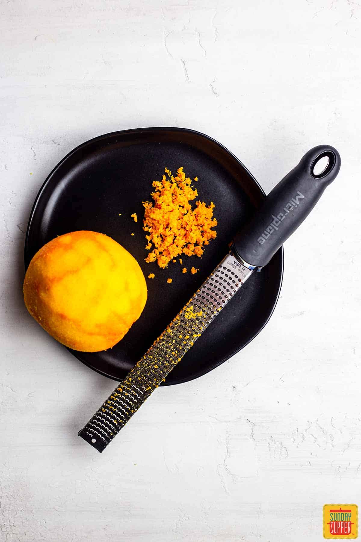 Zest of an orange and an orange on a black plate with a grater