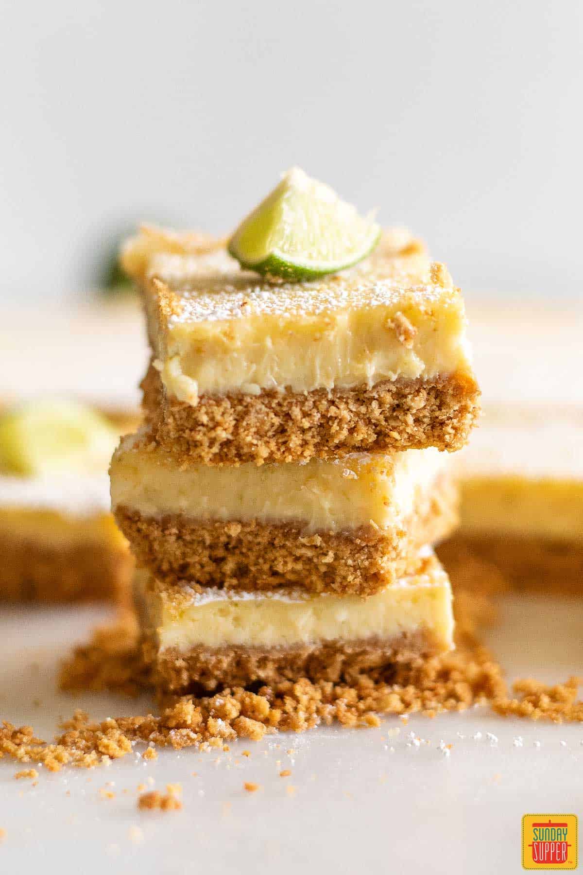 Close up of three key lime pie bars stacked on top of one another with a key lime wedge on top