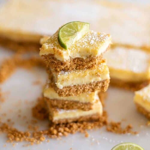 Three key lime pie bars stacked on top of each other surrounded by cookie crumbles with a lime slice on top