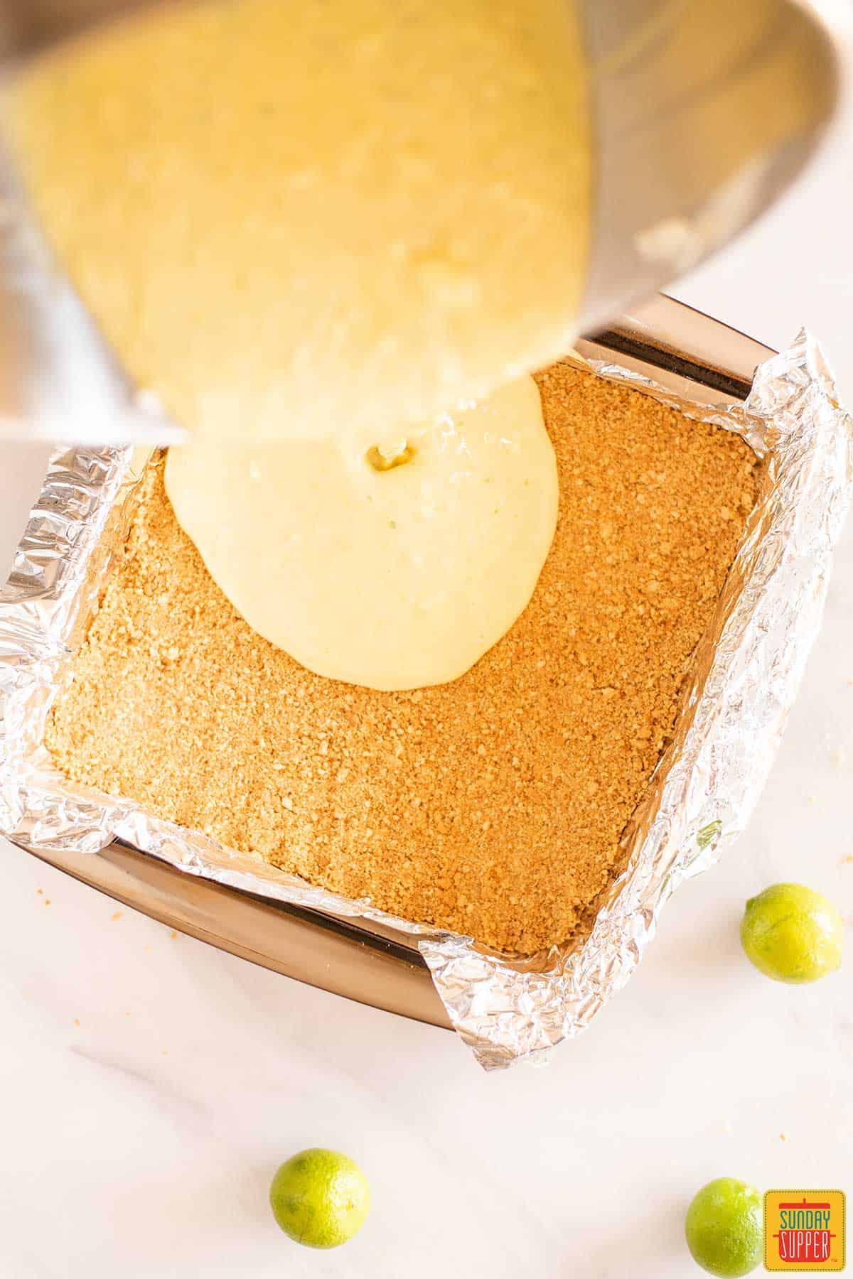 Pouring key lime pie filling into the cookie crust in the foil