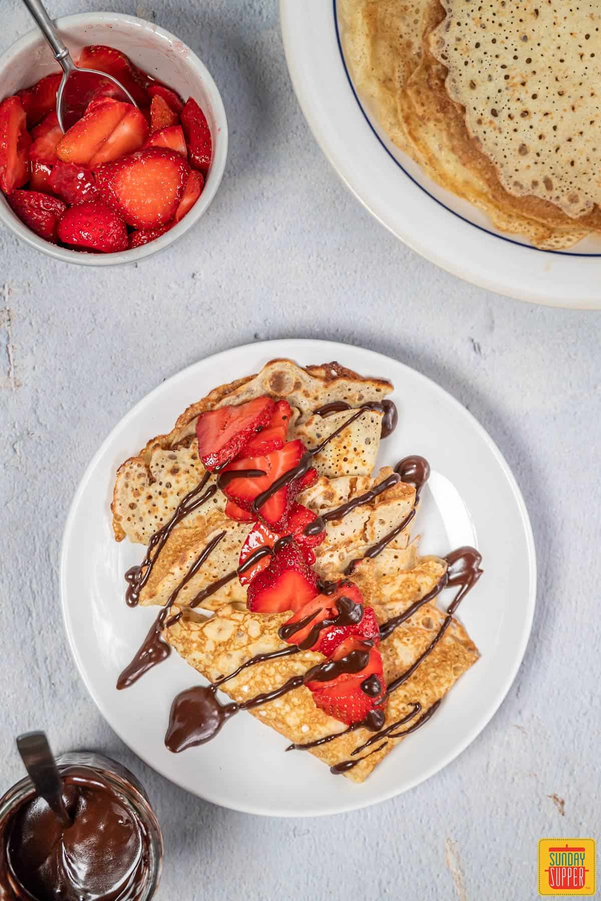 Strawberry crepes on a white plate drizzled with chocolate syrup