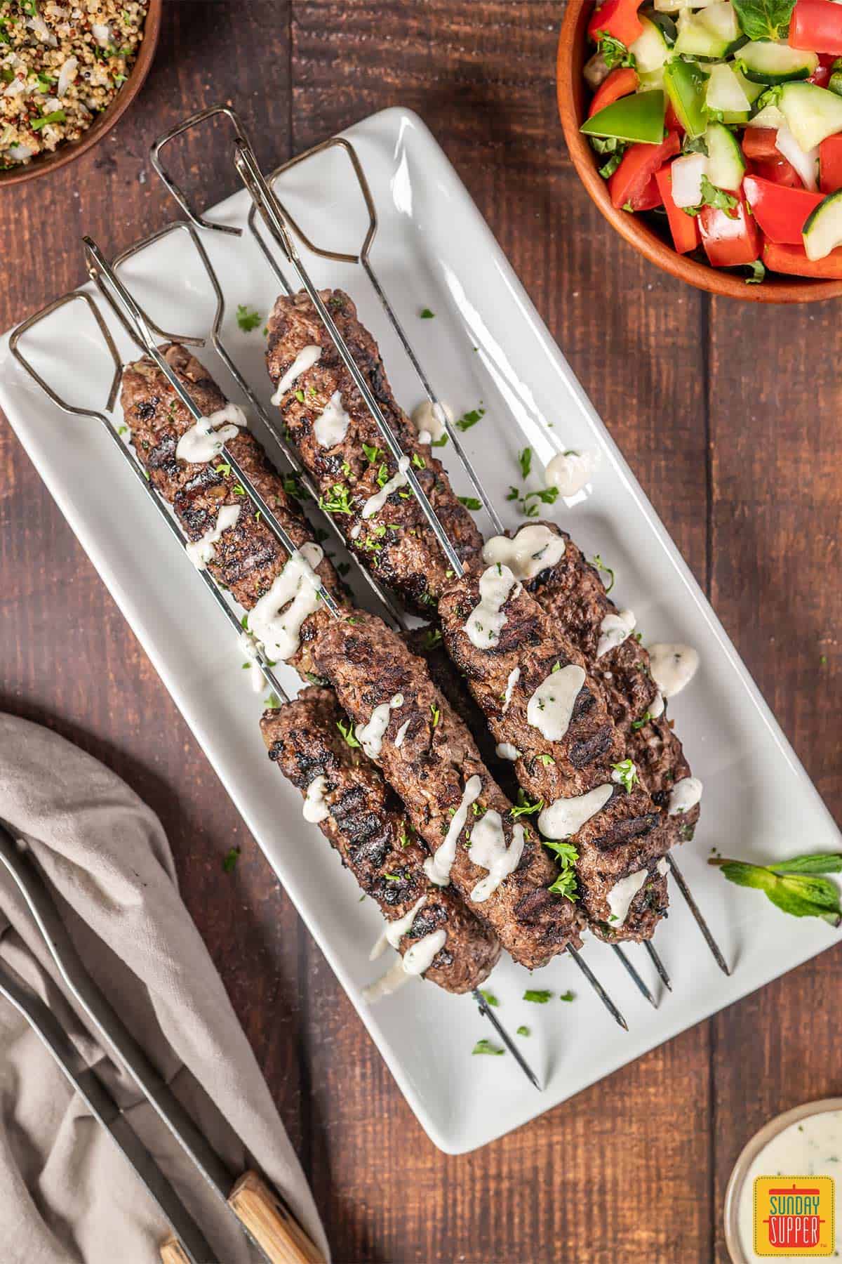 Beef kofta kebabs on a white plate with sauce on top