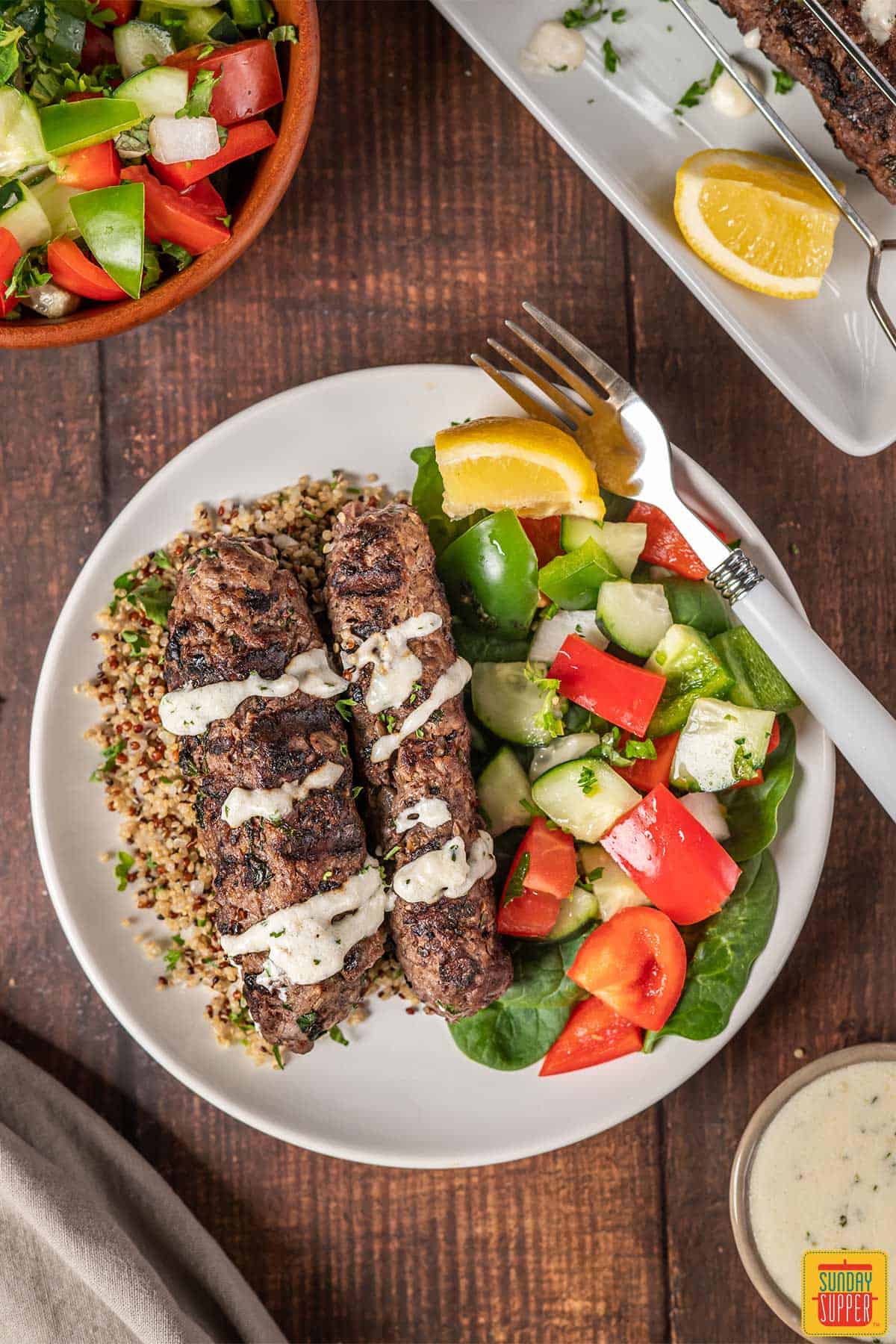 Lebanese beef kofta on a plate with couscous and cucumber salad