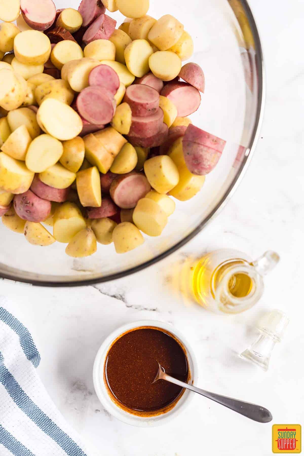 Bowl of sauce mix with a spoon in it next to fingerling potatoes in a glass bowl
