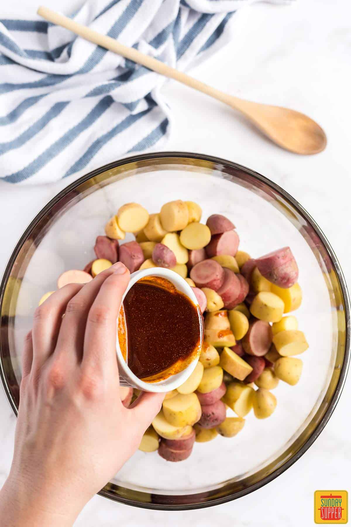 Pouring the sauce for Portuguese potatoes into a bowl of fingerling potatoes