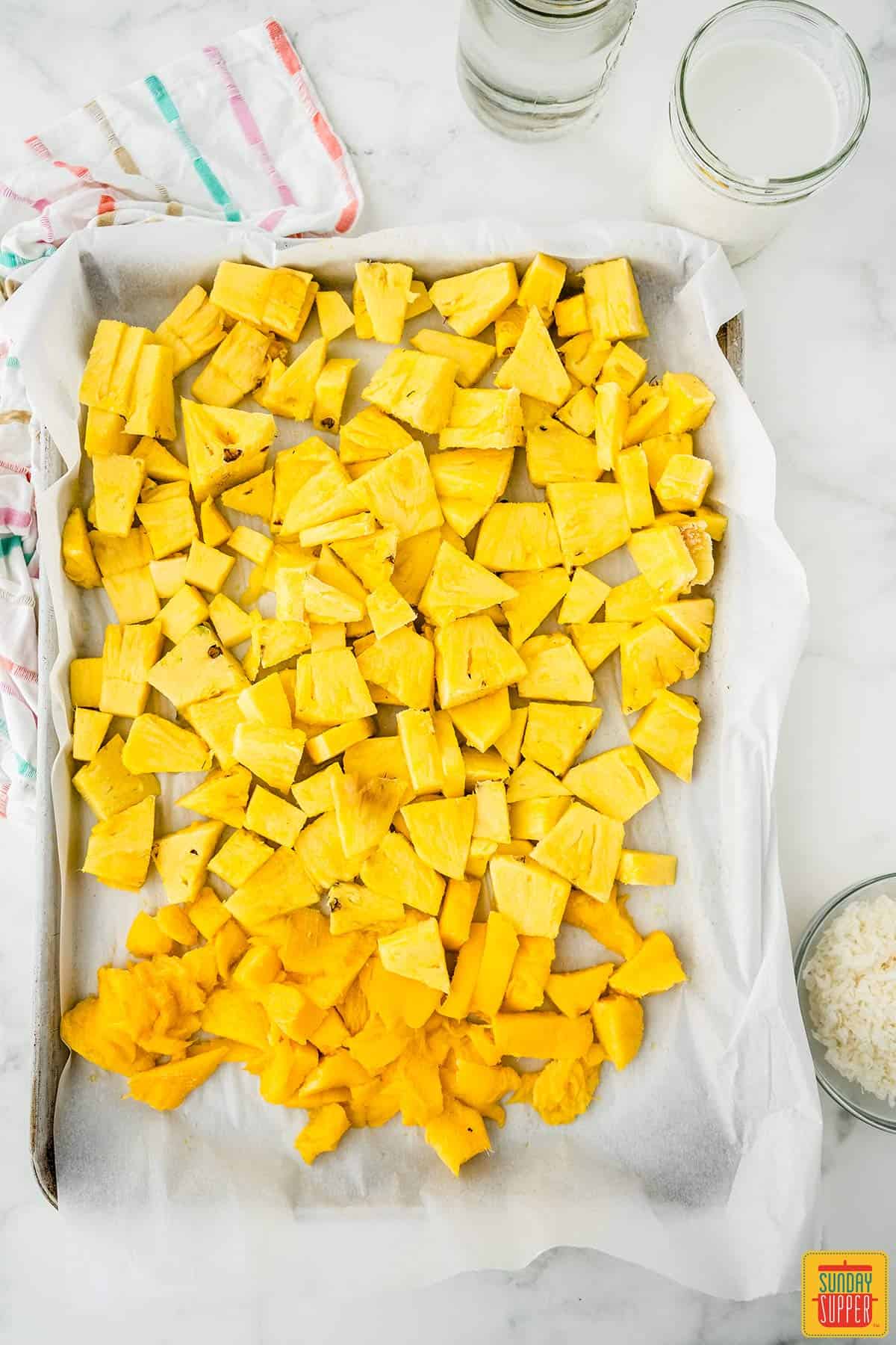 Pineapple and mango slices on a tray next to a bowl of coconut flakes