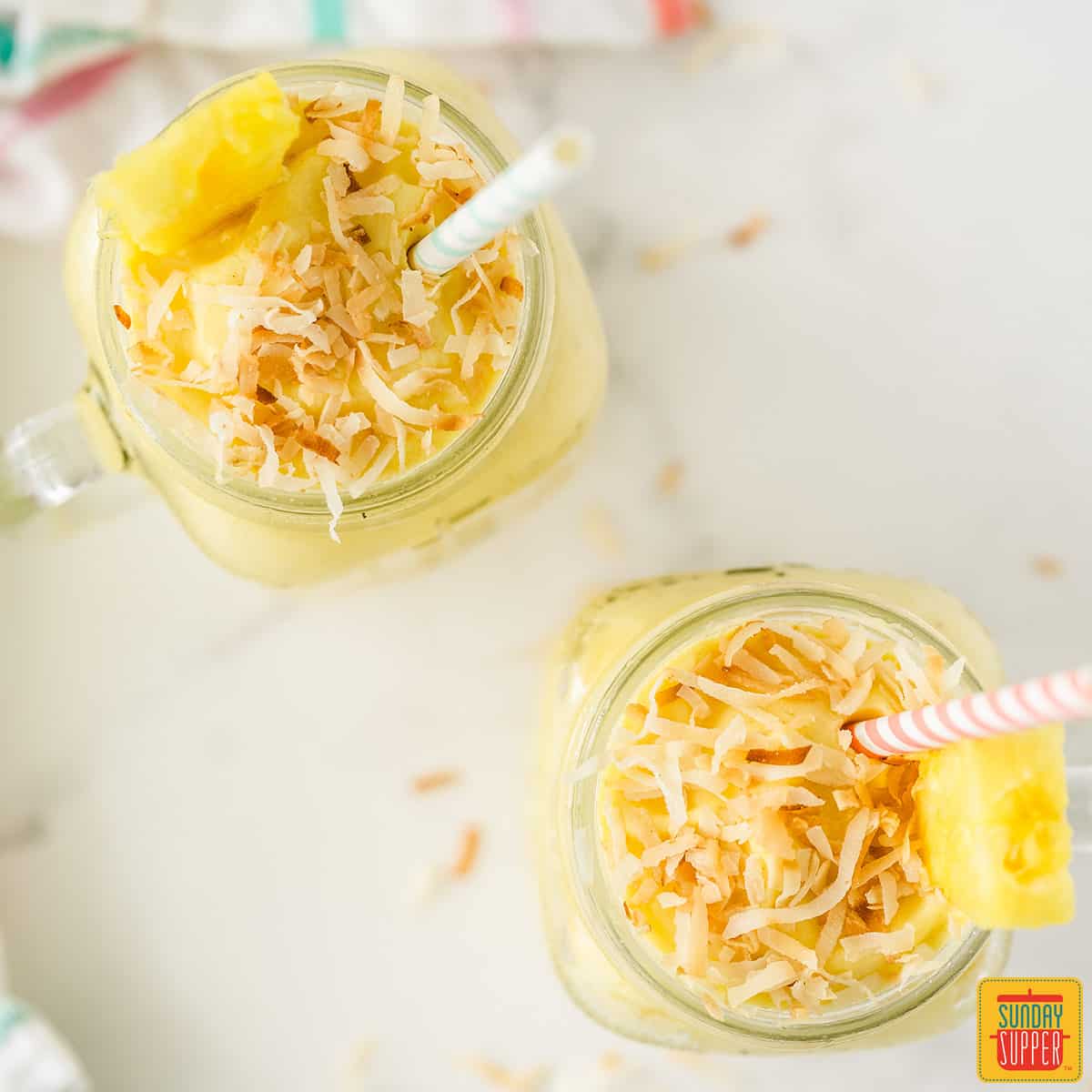 Overhead shot of two tropical rum cocktails with toasted coconut on top and straws