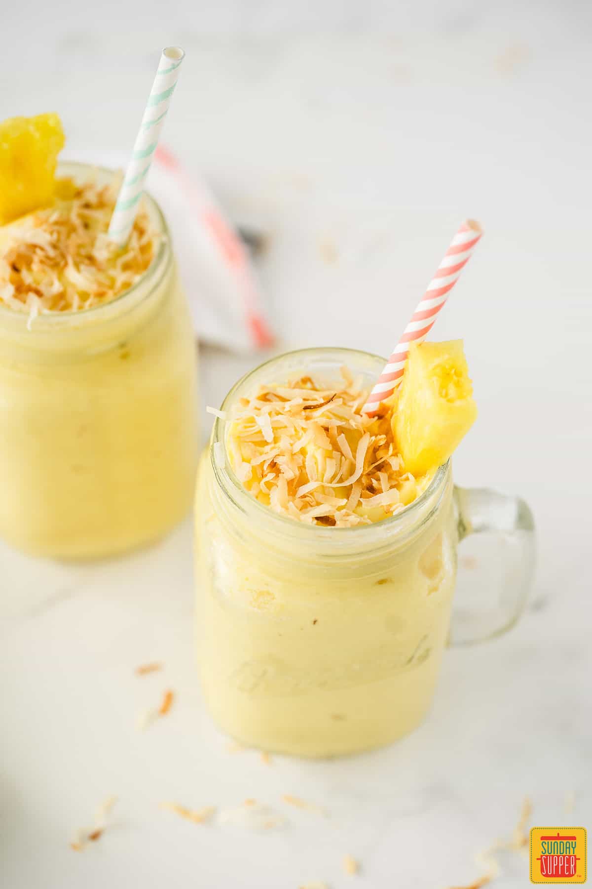 Two glass mason jars of tropical rum cocktail with toasted coconut and pineapple slices