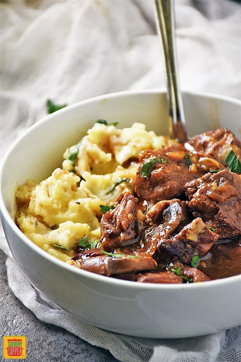 Slow Cooker Beef Tips and Gravy in a white bowl with mashed potatoes