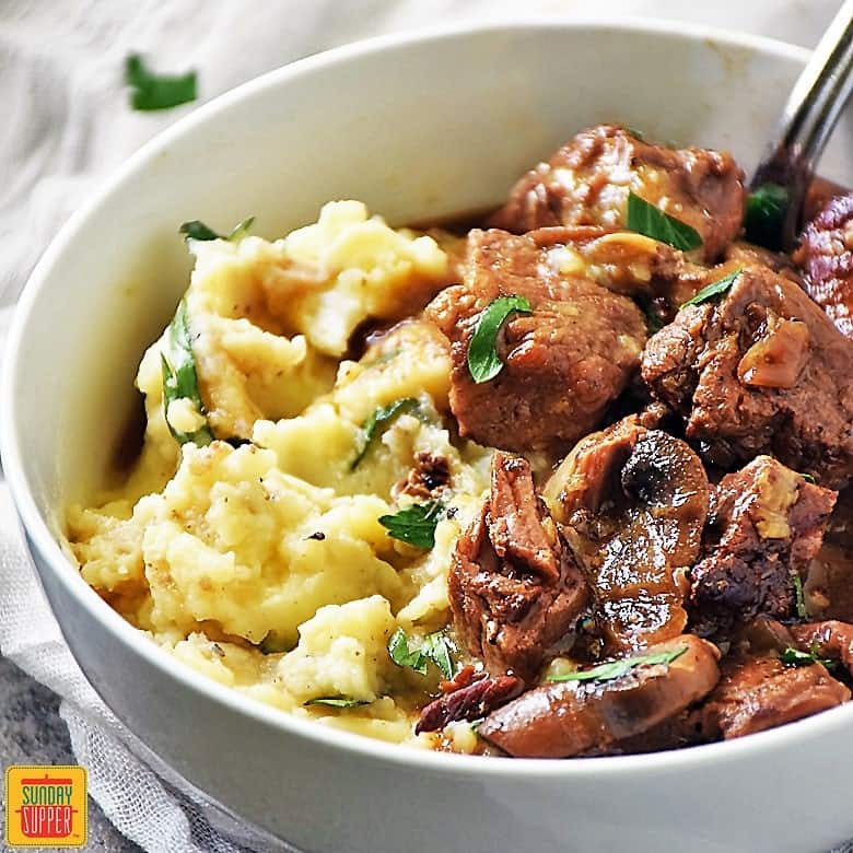 Slow Cooker Beef Tips and Gravy in a white bowl over mashed potatoes
