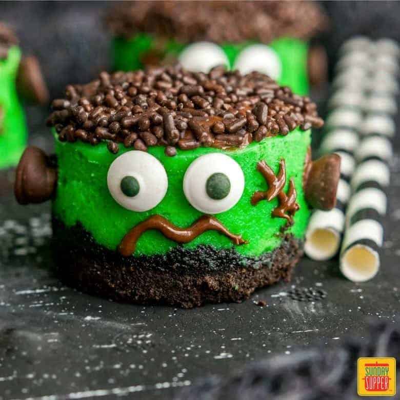 Mini Halloween Cheesecakes decorated like Frankenstein on a black surface