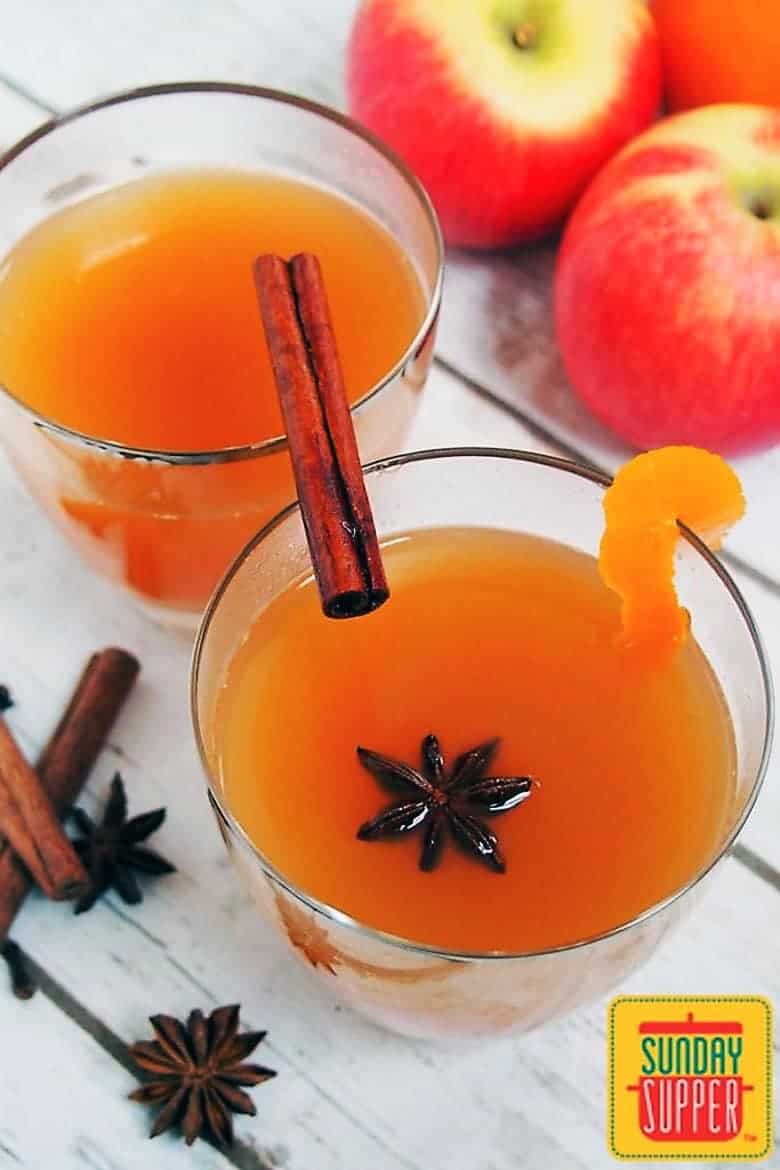 Spiked Mulled Cider in a glass with a cinnamon stick and star anise on a white wooden surface