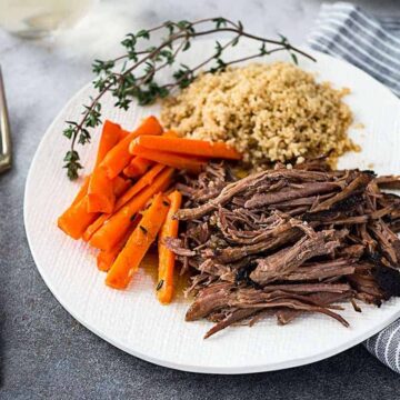 A white plate of slow cooker roast beef with glazed carrots and couscous