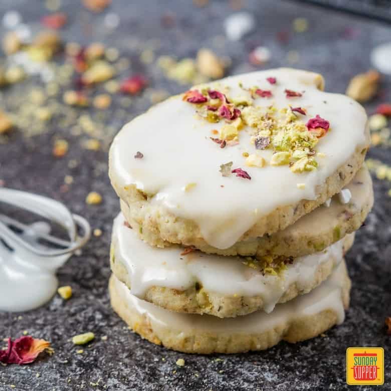 A stack of four orange cardamom cookies with an icing whisk off to the side