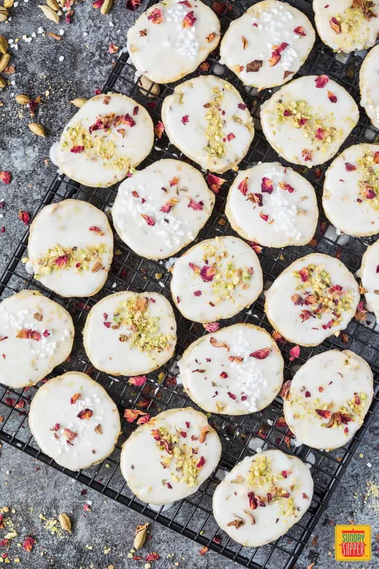 Orange cardamom cookies on a baking rack after adding icing and toppings