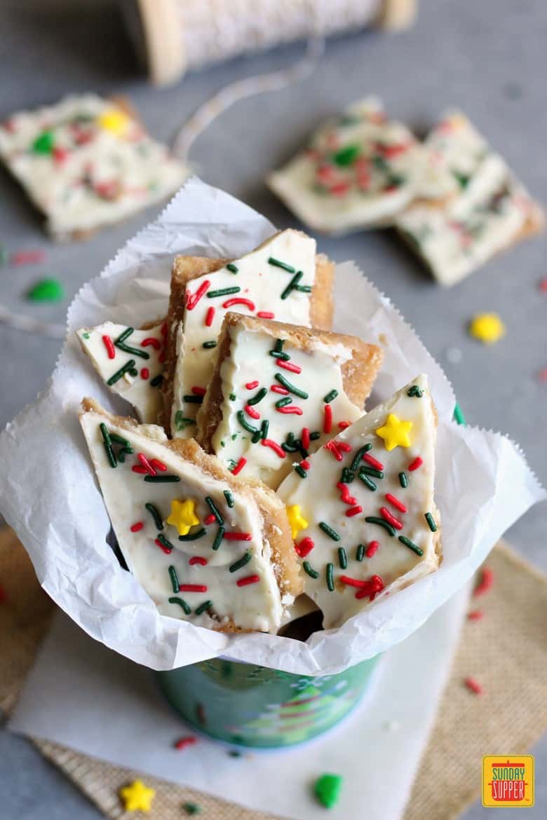 white chocolate saltine toffee bark in white gift paper in a christmas-themed tin