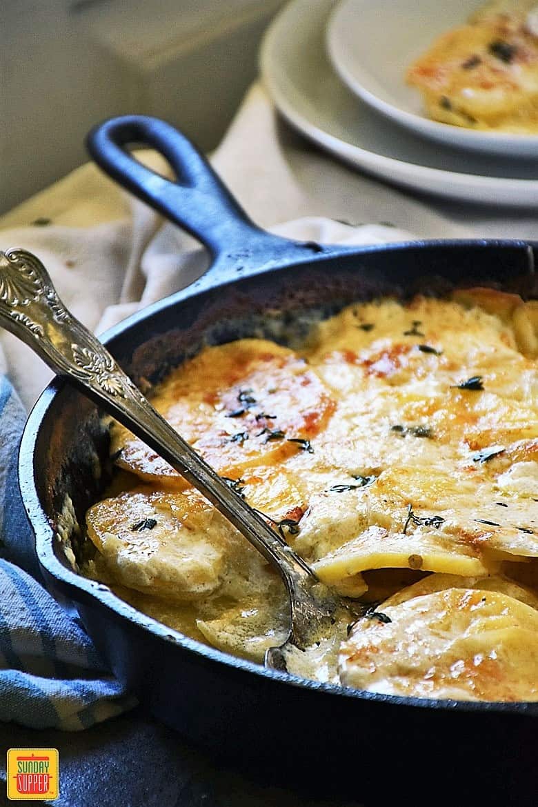 A skillet with gluten free au gratin potatoes and a serving spoon ready to enjoy