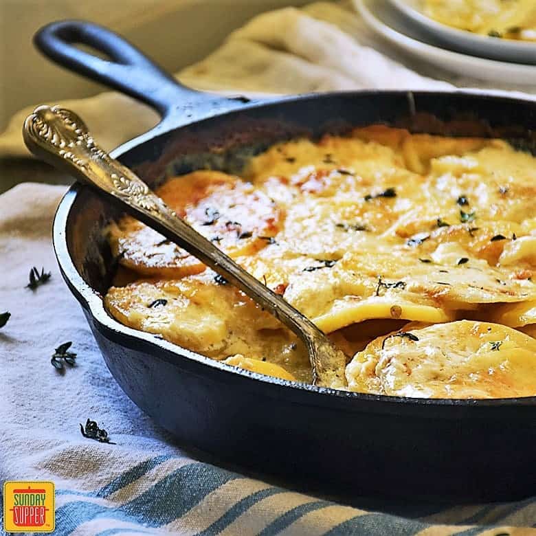 Gluten free au gratin potatoes in a cast iron skillet with a serving spoon