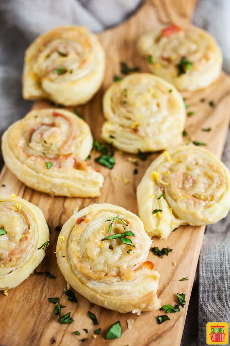 ham and cheese pinwheels topped with basil on a wooden serving board