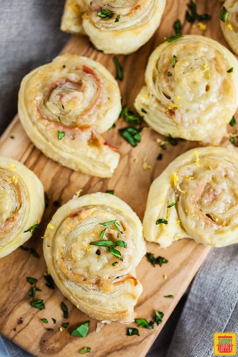 puff pastry ham and cheese pinwheels on a wooden serving board with basil