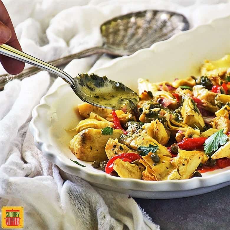 Drizzling basil vinaigrette with a spoon onto roasted artichoke salad