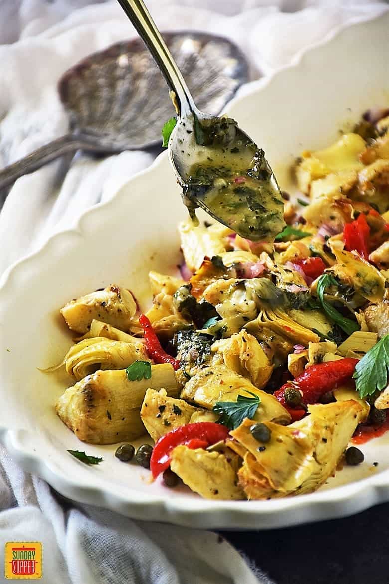 Pouring vinaigrette over roasted artichokes salad using a spoon