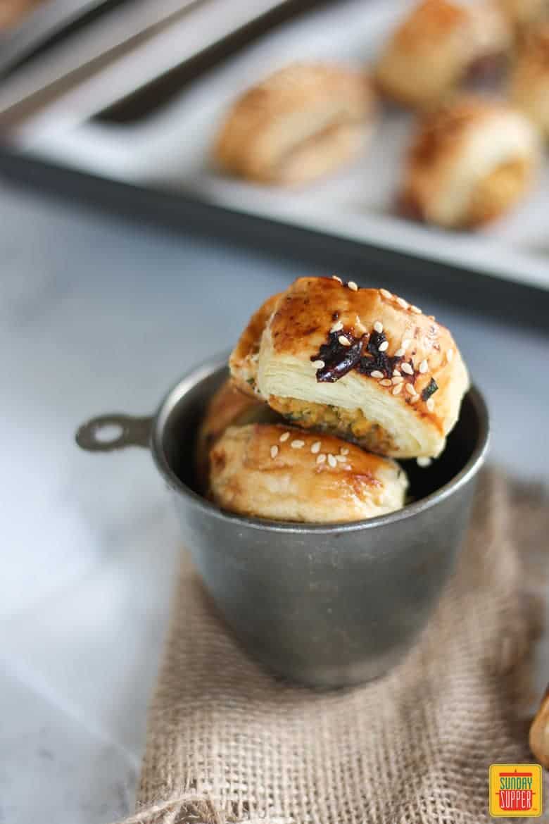 Chicken Sausage Rolls in a cup by a baking sheet of sausage rolls