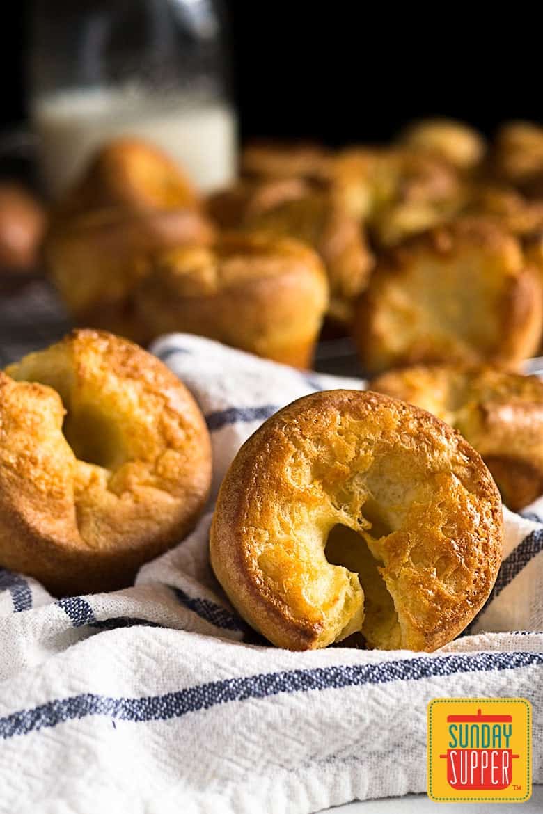 Close up of two yorkshire puddings in front of the blurred batch from the yorkshire pudding recipe