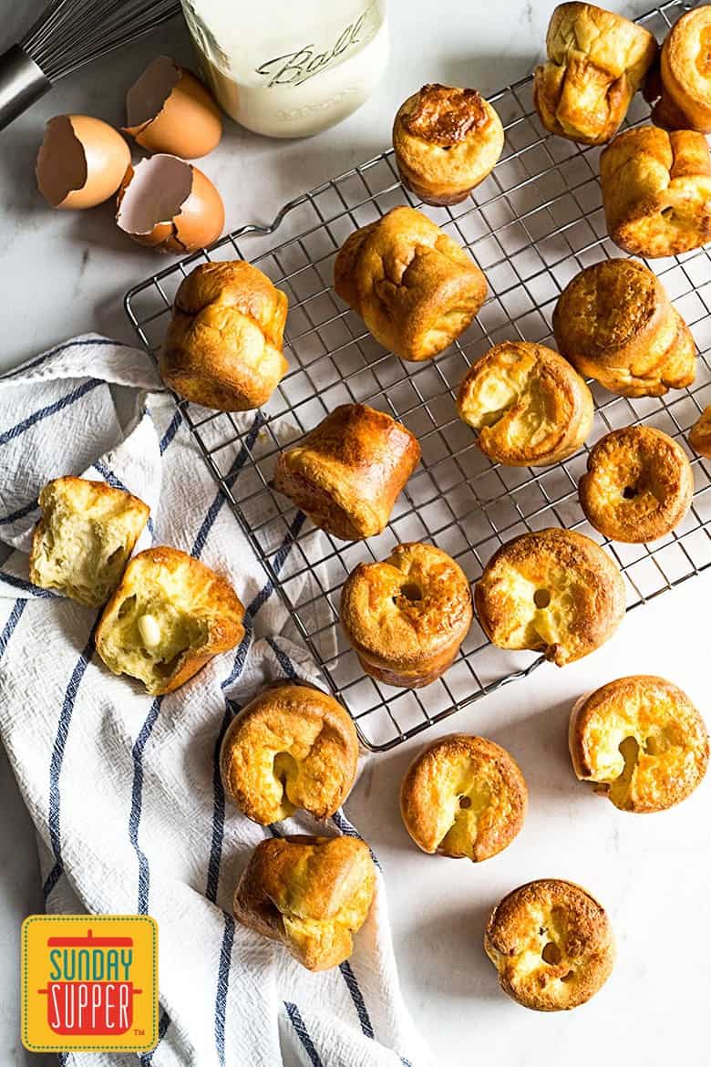 Freshly baked yorkshire pudding recipe on a baking rack on a white surface, next to cracked eggs and a milk glass