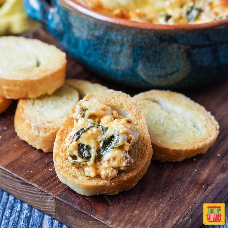 Chorizo cheese dip on little slices of toast topped with dip on a wooden surface