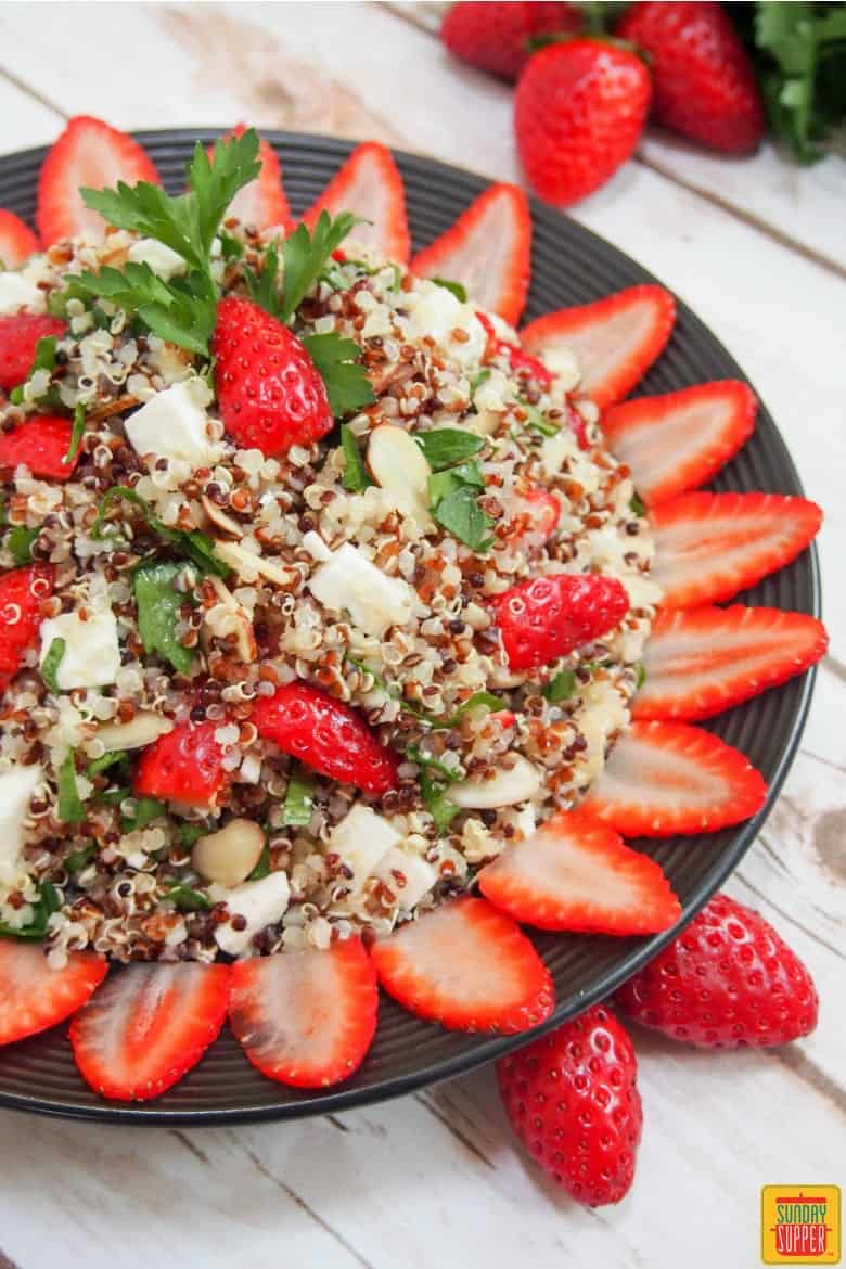 strawberry quinoa salad served on a black plate with fresh strawberries