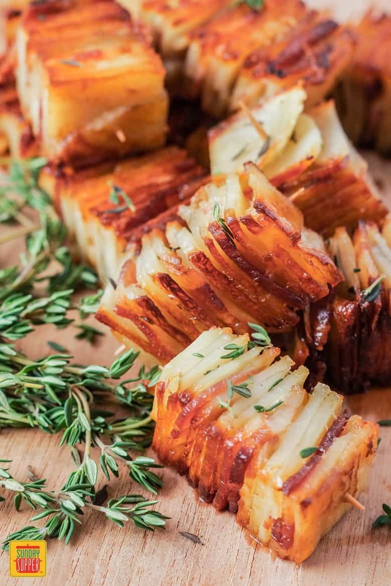 Stacks of potato pave with bacon and parmesan and fresh herbs on a wooden surface