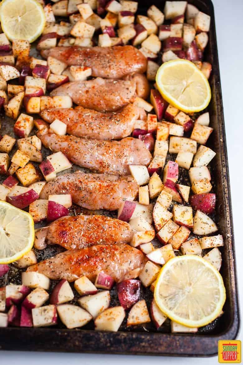 Chicken surrounded by potatoes and lemons on a baking sheet