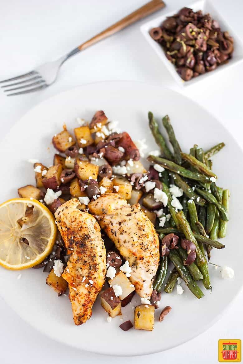 Greek lemon chicken and potatoes on a plate with feta cheese and green beans