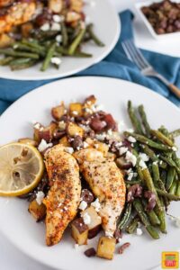 Greek chicken and potatoes on a plate with green beans and a lemon slice