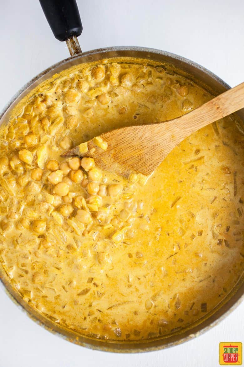 Chickpea curry in a skillet with a wooden spatula