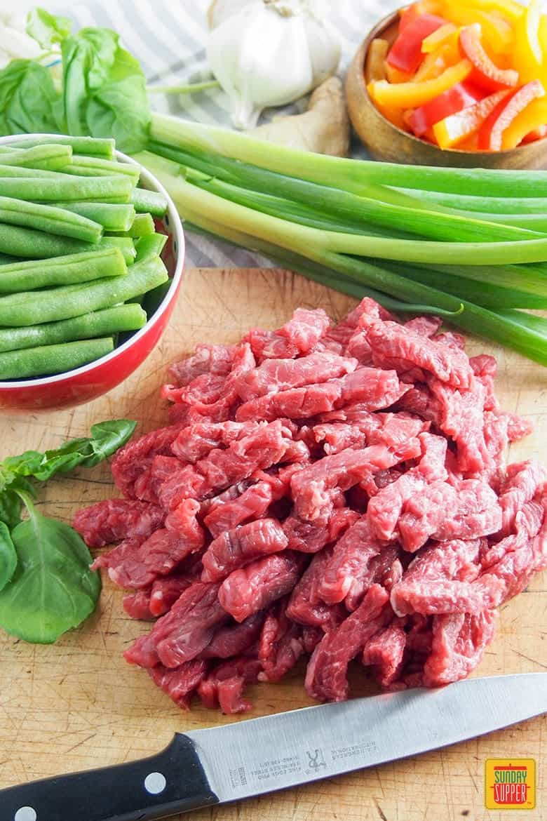 Asian beef stir fry ingredients on a cutting board with a knife