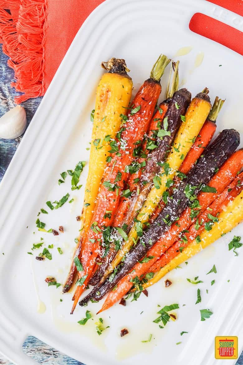 Garlic parmesan roasted carrots on a white platter with fresh herbs