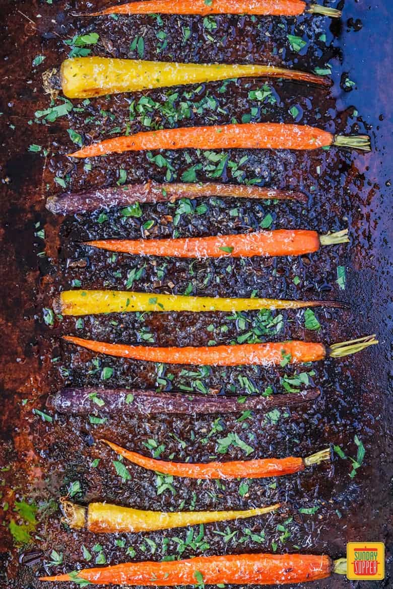 Rainbow carrots on baking sheet, roasted and ready to eat. Garnished with parsley and Parmesan cheese