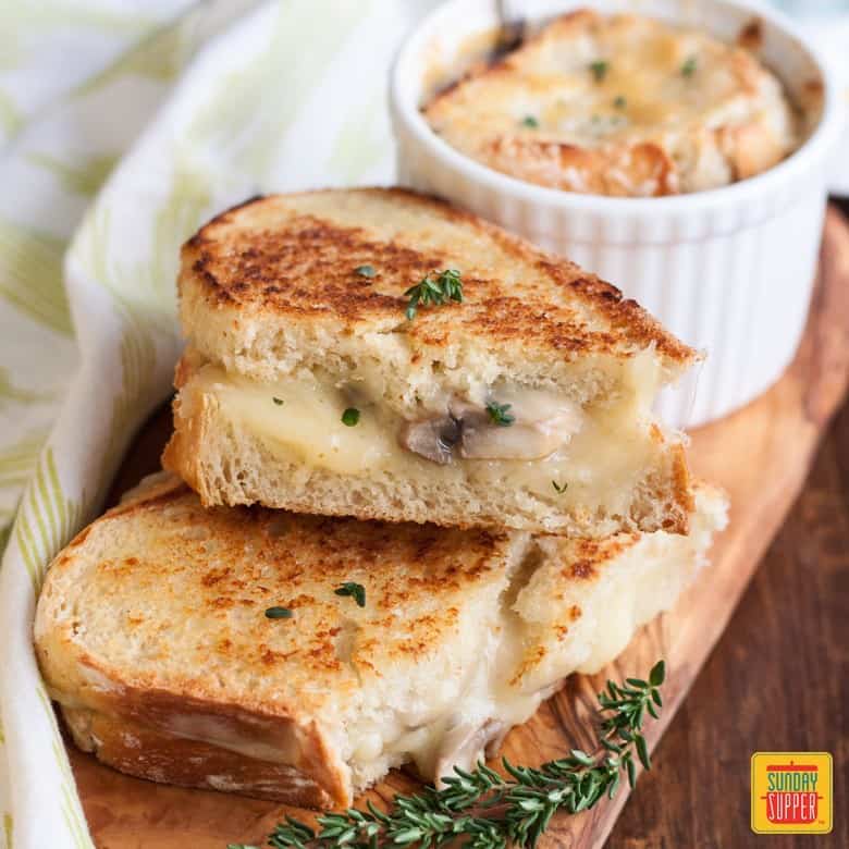 Mushroom grilled cheese sandwich with french onion soup in a ramekin on a wooden board for serving