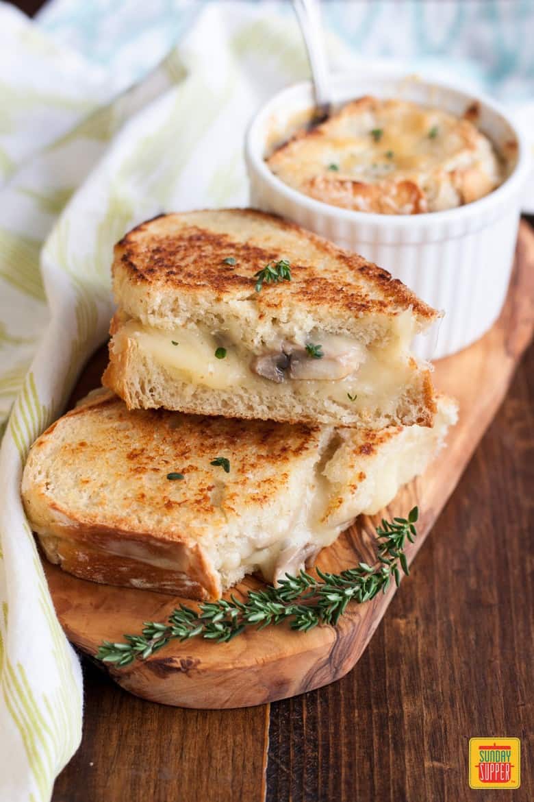 Mushroom grilled cheese and french onion soup in a ramekin on top of a small wooden cutting board for serving