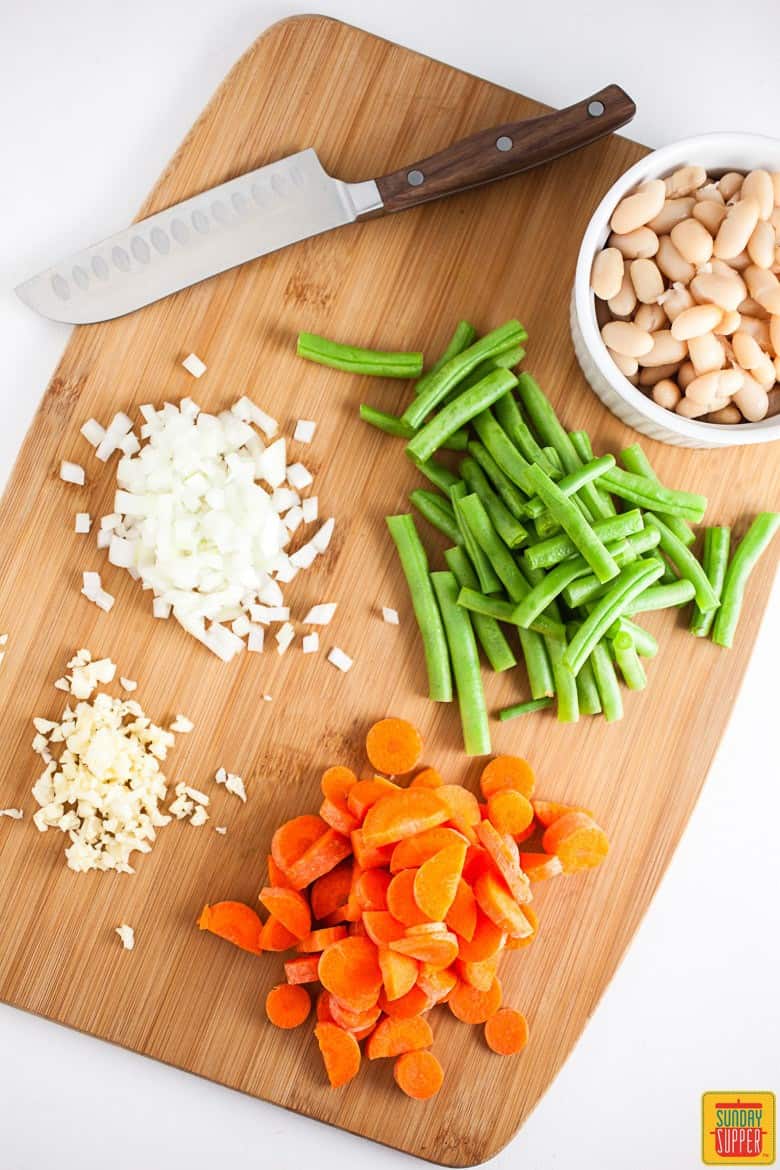 Cutting board topped with chopped vegetables for the Italian Vegetable Soup and Pesto Grilled Cheese recipe
