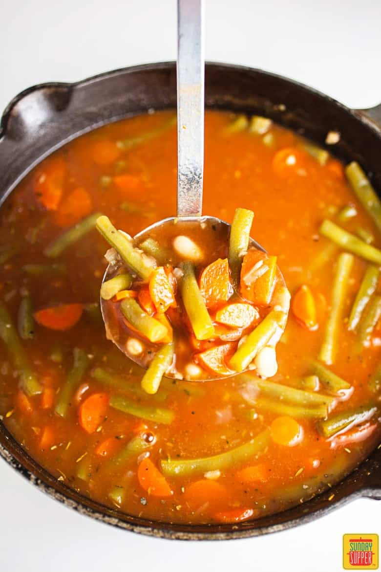 Pot of Italian Vegetable Soup with a full ladle ready to serve with Pesto Grilled Cheese