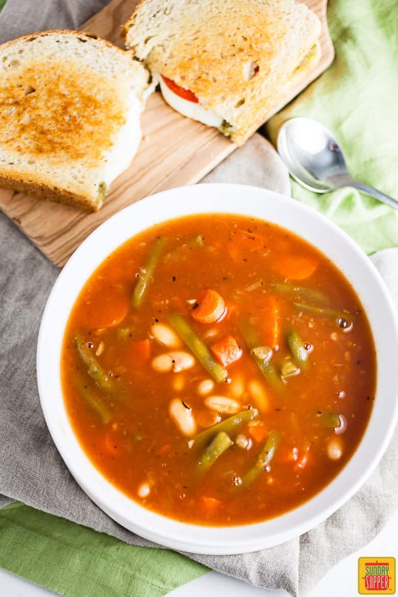 Italian vegetable soup in a bowl next to pesto grilled cheese