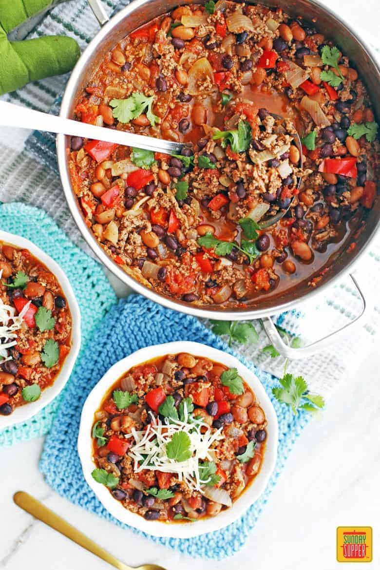Two bowls of easy ground beef chili next to a pot of chili with a serving ladle