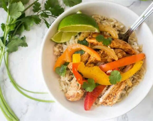Chicken Fajitas and rice in a white bowl with a spoon and cilantro garnish